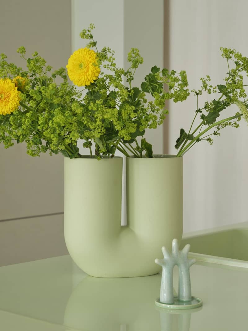 Eine symmetrische Vase mit zwei &Ouml;ffnungen ist mit gelben und gr&uuml;nen Blumen best&uuml;ckt